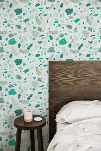 Faux Green Terrazzo peel and stick wallpaper with scattered green and gray terrazzo chips beside a dark wood bed headboard.