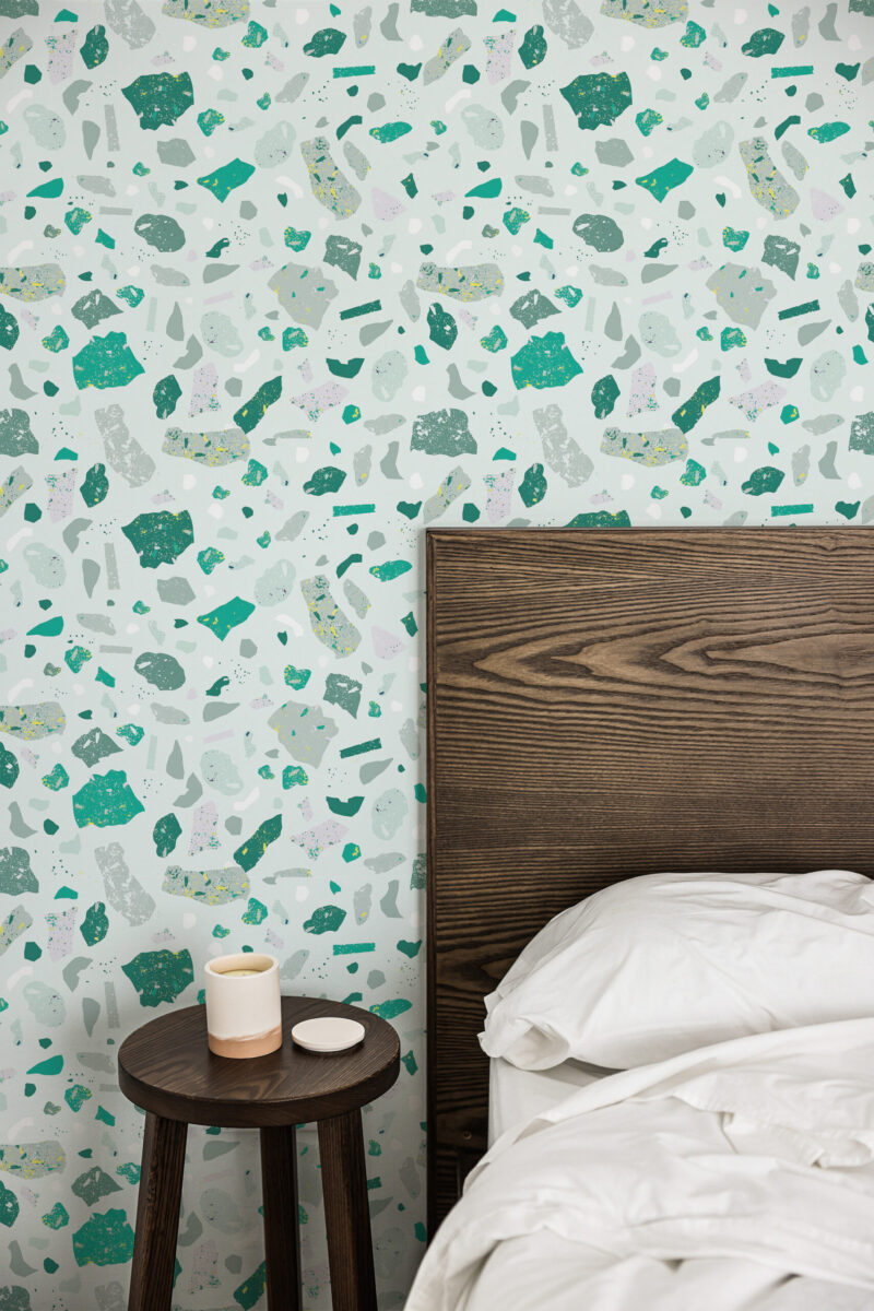 Faux Green Terrazzo peel and stick wallpaper with scattered green and gray terrazzo chips beside a dark wood bed headboard.
