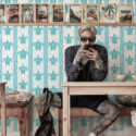 Coastal Tribal Turtles non-pasted wallpaper with turquoise turtles and wavy stripes behind a wall of magazine shelves.