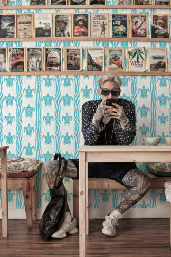Coastal Tribal Turtles non-pasted wallpaper with turquoise turtles and wavy stripes behind a wall of magazine shelves.