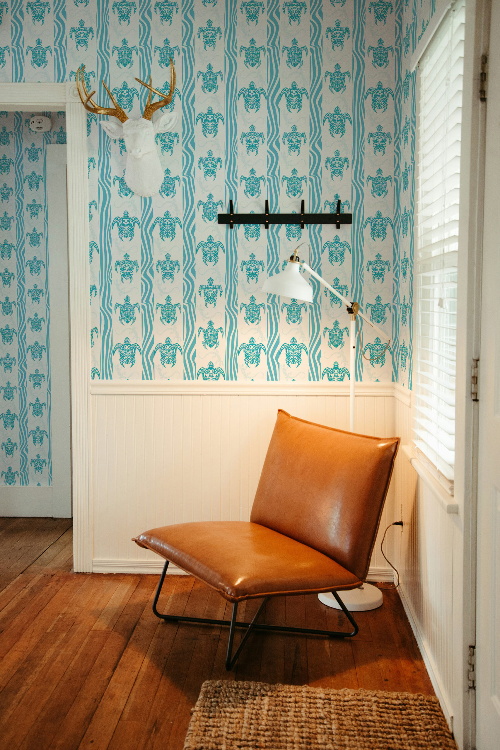 Coastal Tribal Turtles pre-pasted wallpaper with teal turtles and wavy stripes covering a corner wall near a window.