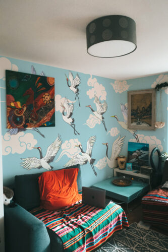 Flying Cranes Chinoiserie Blue covers the bedroom corner in a wall mural of white cranes soaring through cloud shapes.