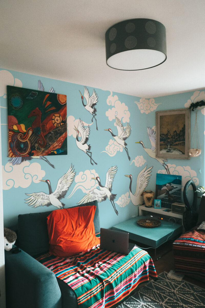 Flying Cranes Chinoiserie Blue covers the bedroom corner in a wall mural of white cranes soaring through cloud shapes.