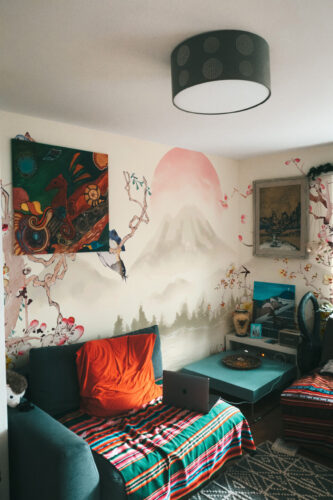 Misty Mountain Sunrise wall mural behind a bed, showing soft misty peaks and a pale pink sunrise with delicate branches.