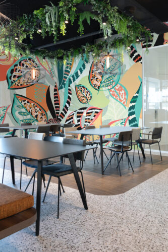 Animal Print Tropical Leaves peel and stick mural wallpaper covers a full wall in a modern café seating area with colorful leaf and animal patterns.