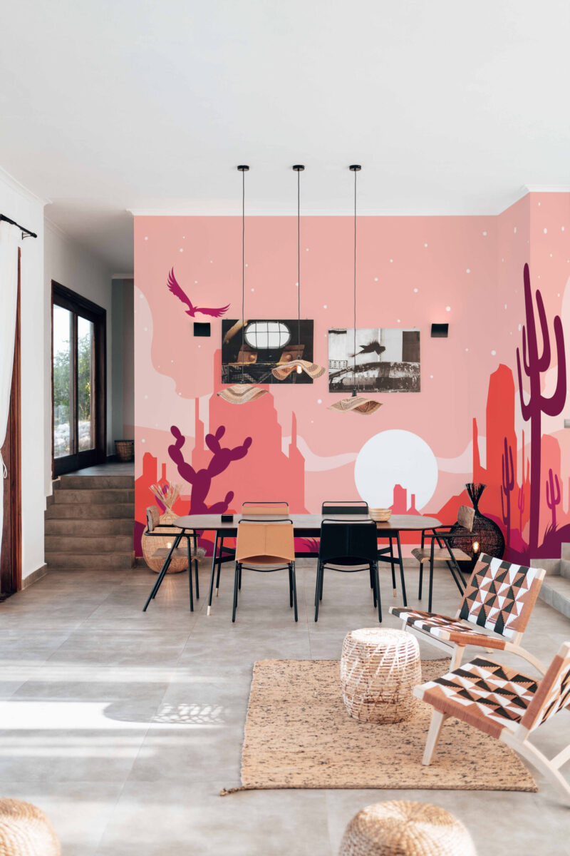 Pink Desert Sunset wall mural spans a dining room wall with cactus silhouettes, distant mesas, and a pale sun on pink sky.