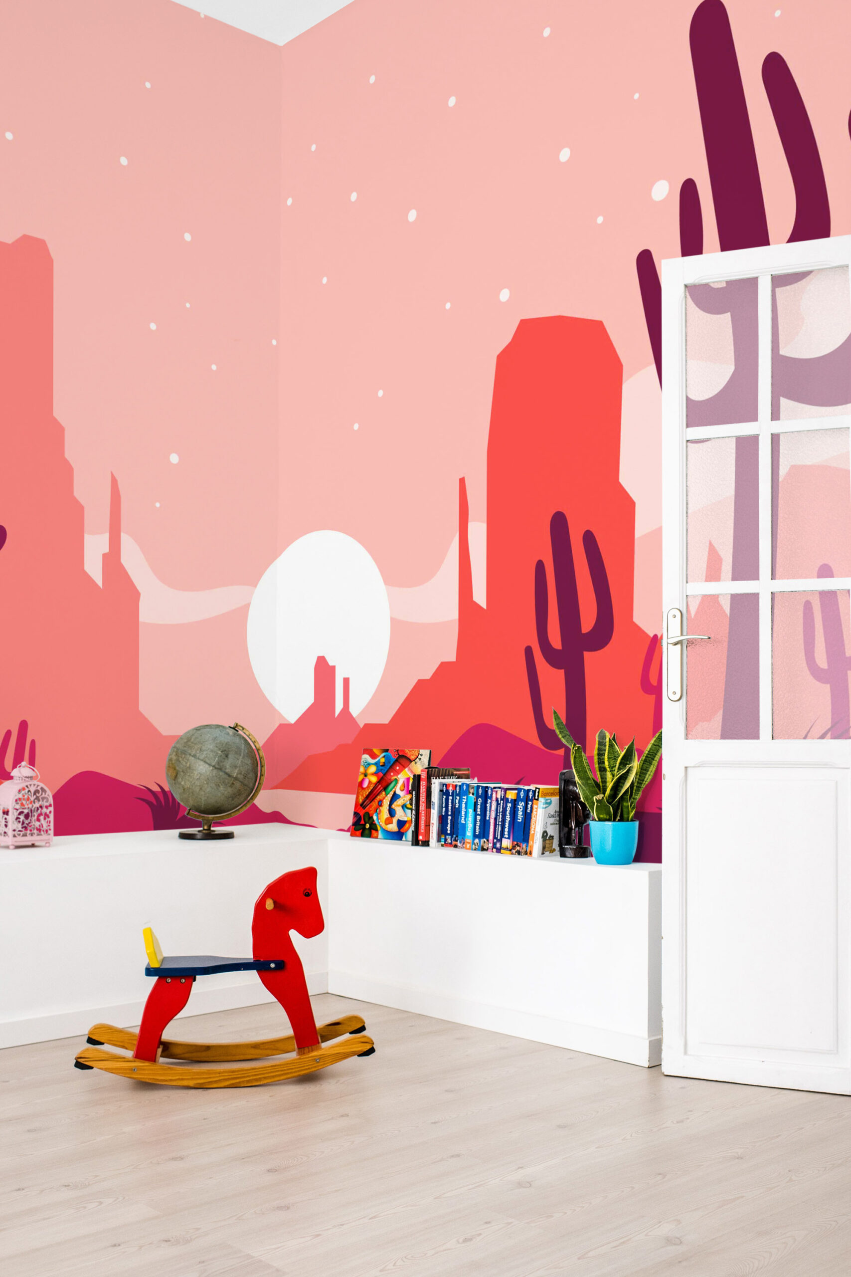 Pink Desert Sunset wall mural covering a corner wall with cactus silhouettes, red mesas, and a pale sun in a kids room.