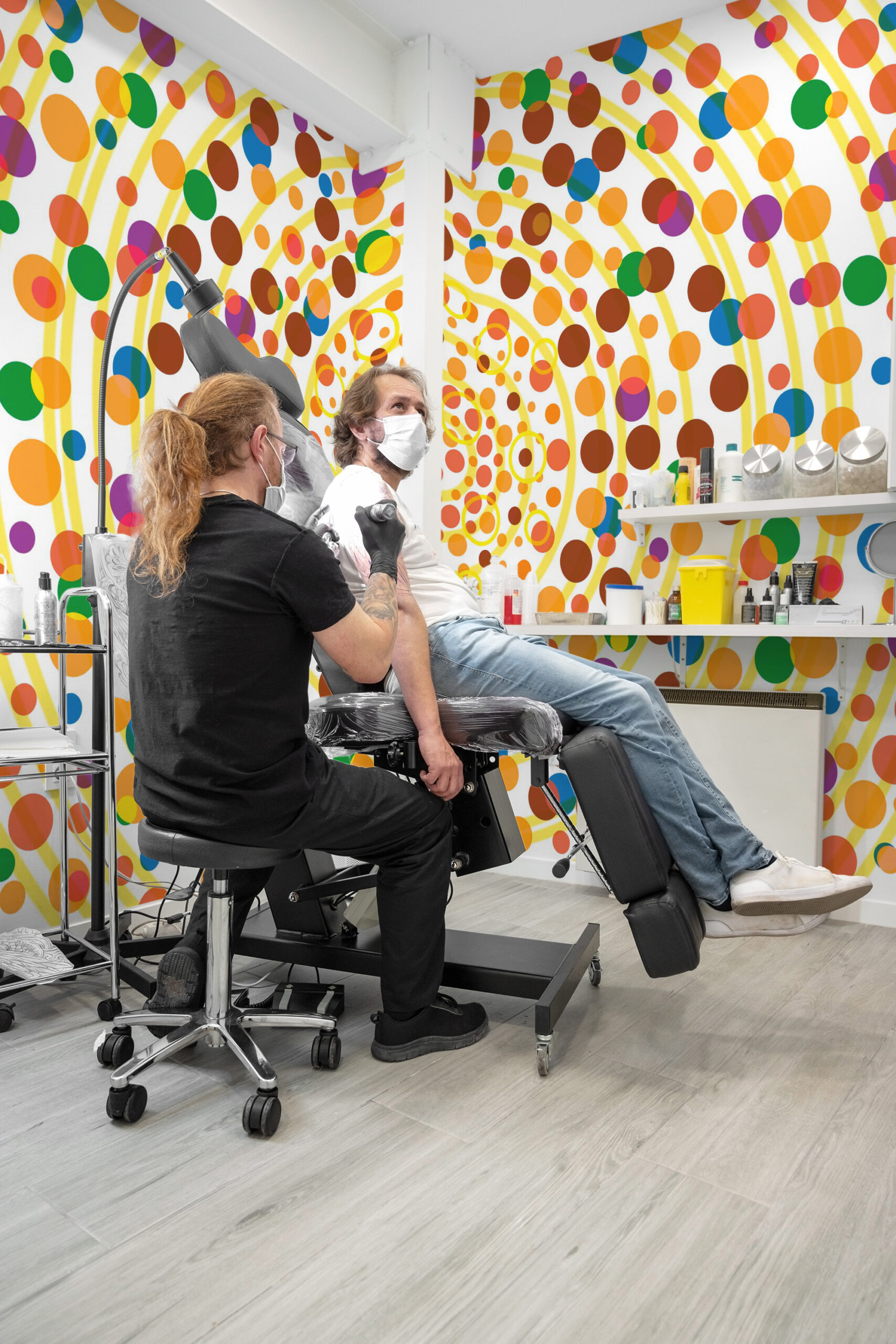 Yellow Dot Vortex wraps a tattoo studio corner as a wall mural, with swirling yellow arcs and multicolored dots.