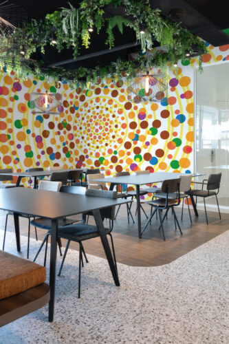 Yellow Dot Vortex peel and stick wall mural fills a modern cafe seating area with a swirling pattern of colorful dots and yellow rings.