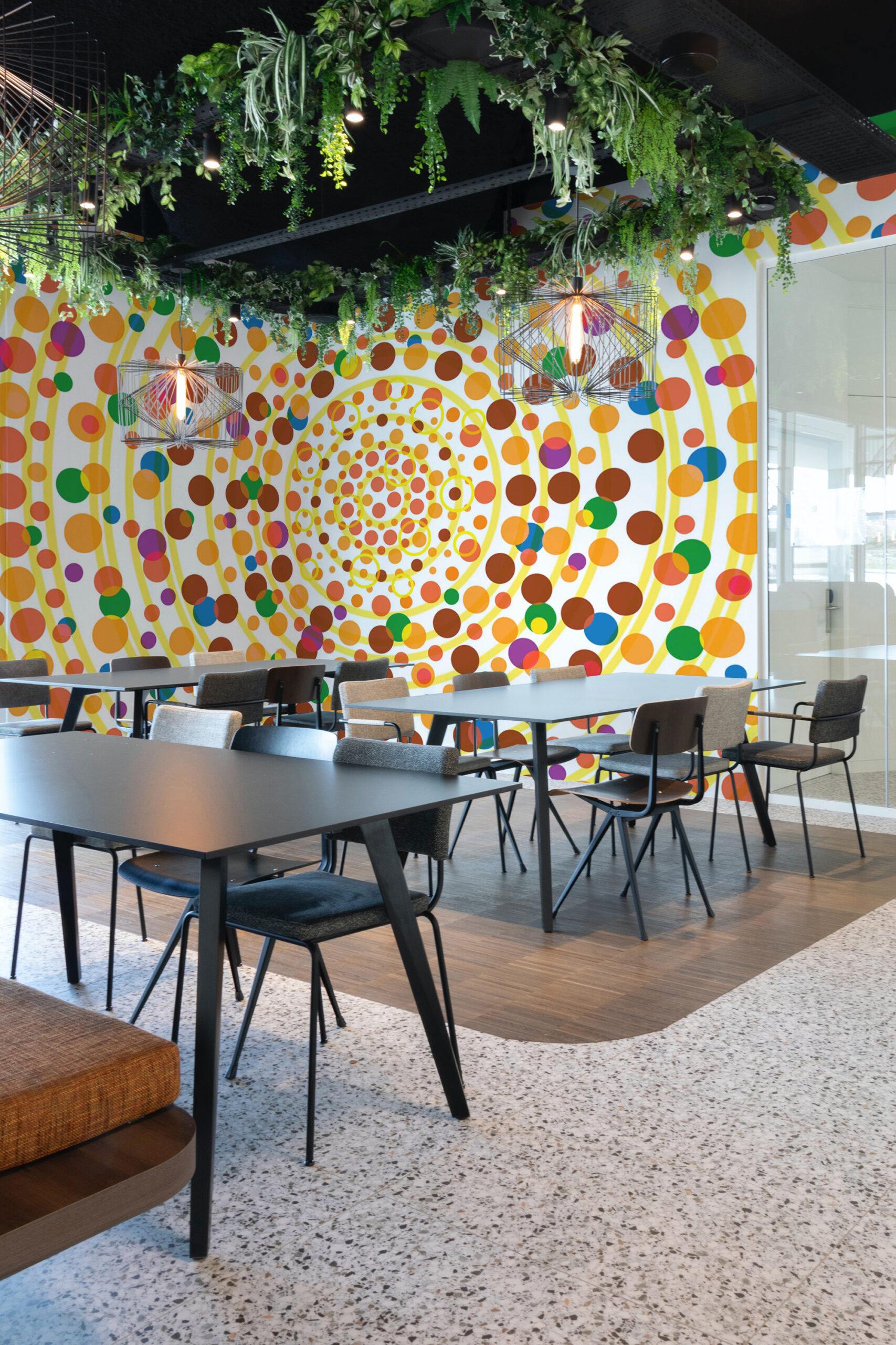 Yellow Dot Vortex peel and stick wall mural fills a modern cafe seating area with a swirling pattern of colorful dots and yellow rings.