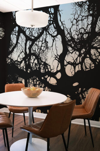 Moody Branch Canopy wall mural spans the dining room accent wall with bold black branches over a pale sky gradient.