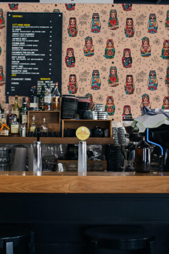 Lucky Charm Tattoo Dolls non-pasted wallpaper with colorful tattoo dolls and doodle icons covering the wall behind the bar.