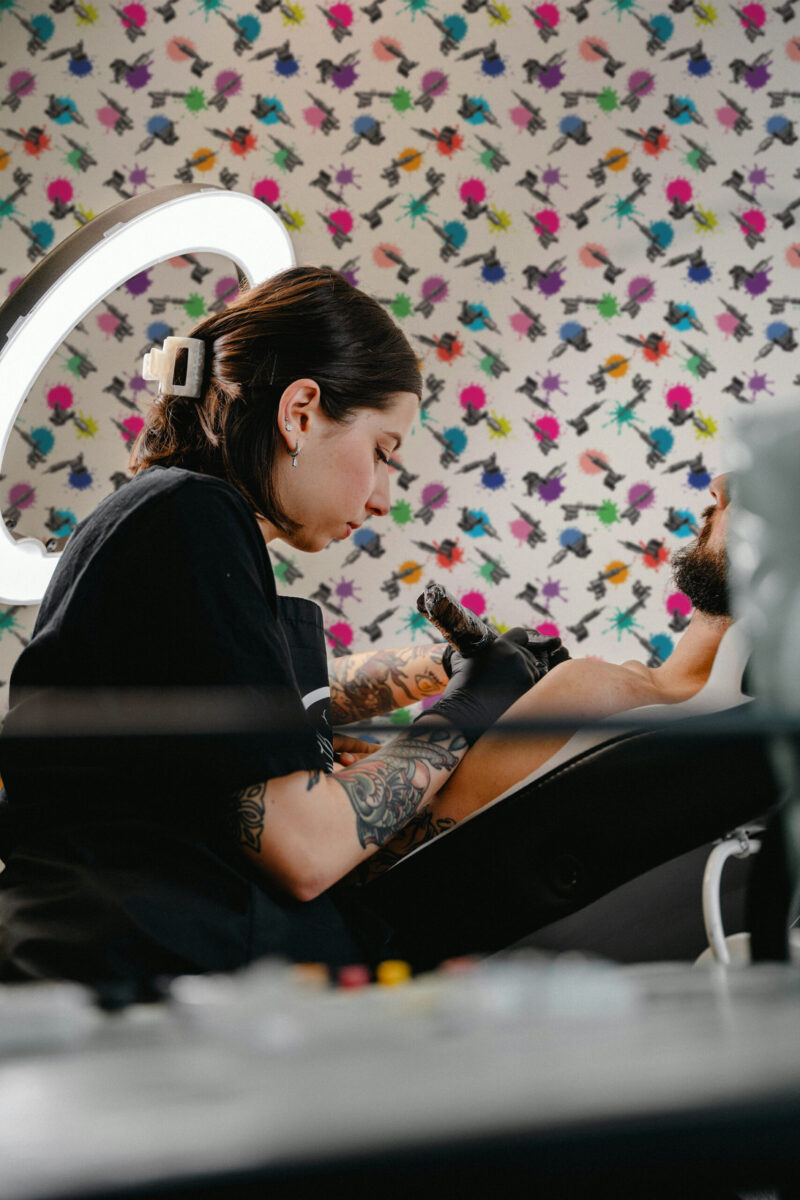 Bold Colorful Tattoo Machine pre-pasted wallpaper with scattered black tattoo machines and bright paint splatters on gray.