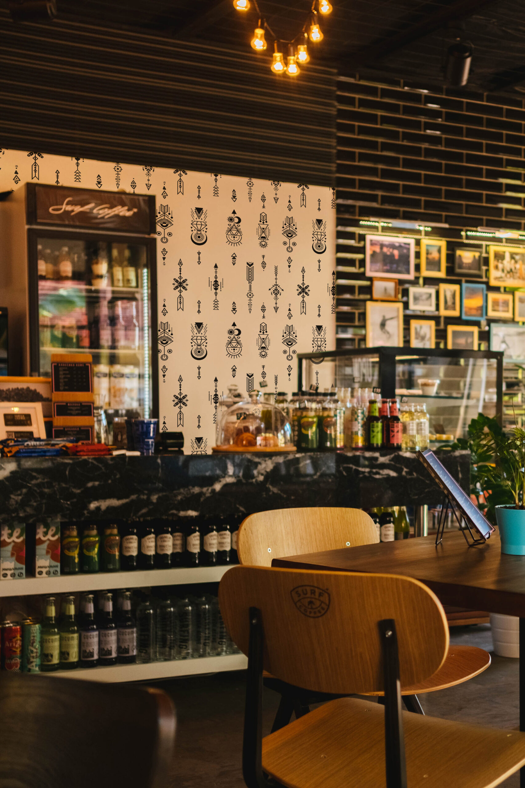 Sacred Tattoo Sigils peel and stick wallpaper with black geometric symbols on beige, shown as an accent wall in a cafe.