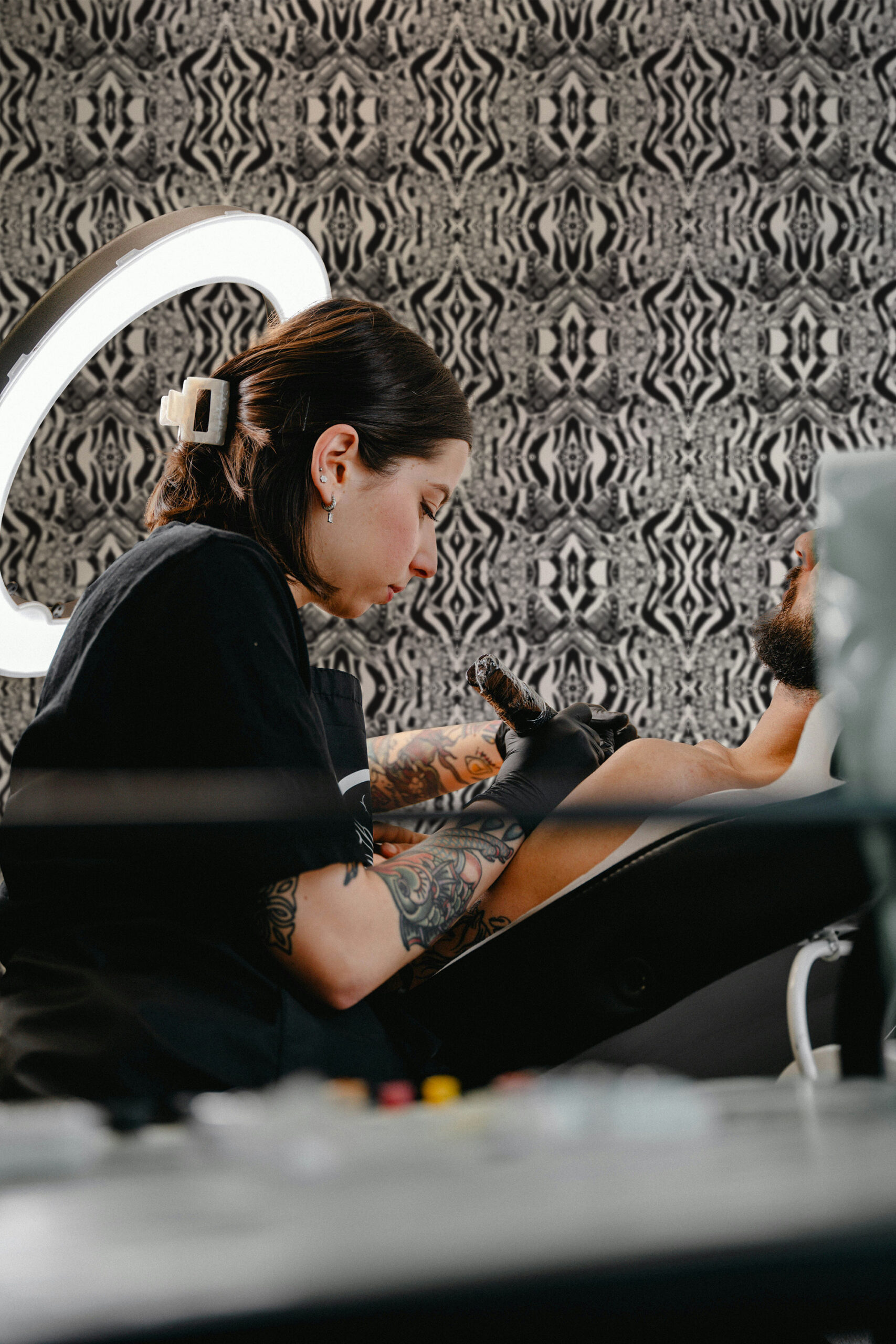 Vintage Black Tattoo Machine pre-pasted wallpaper with a black and gray mirrored pattern covering the wall behind a tattoo chair.