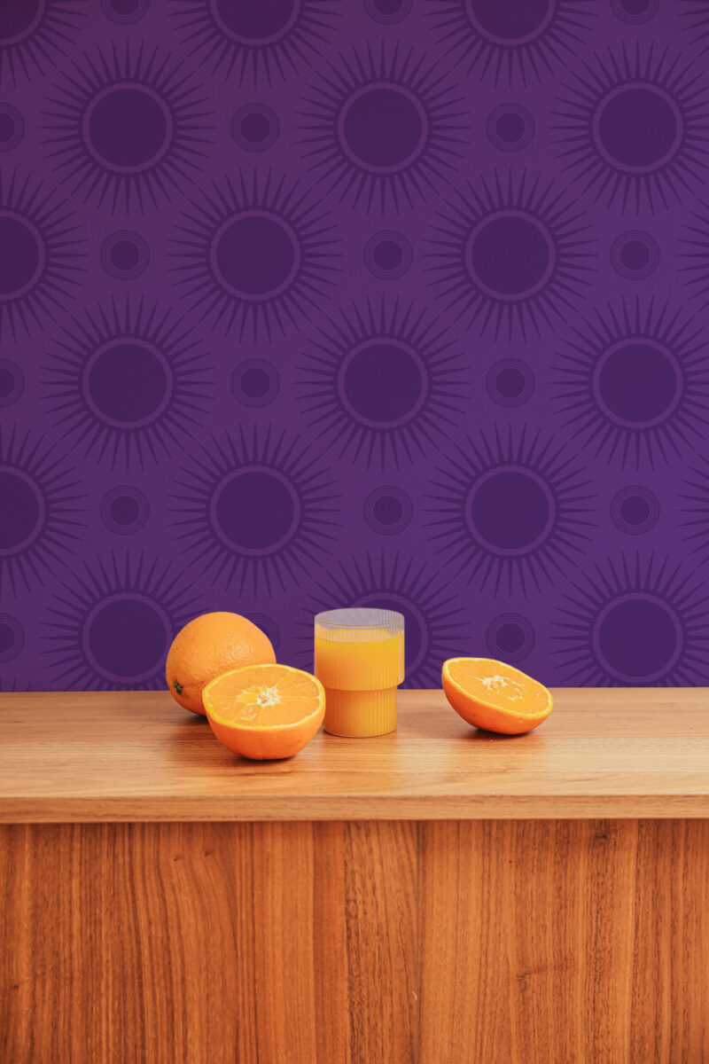 Bold Purple Sunburst peel and stick wallpaper with oversized deep purple sunbursts behind a wooden counter and oranges.