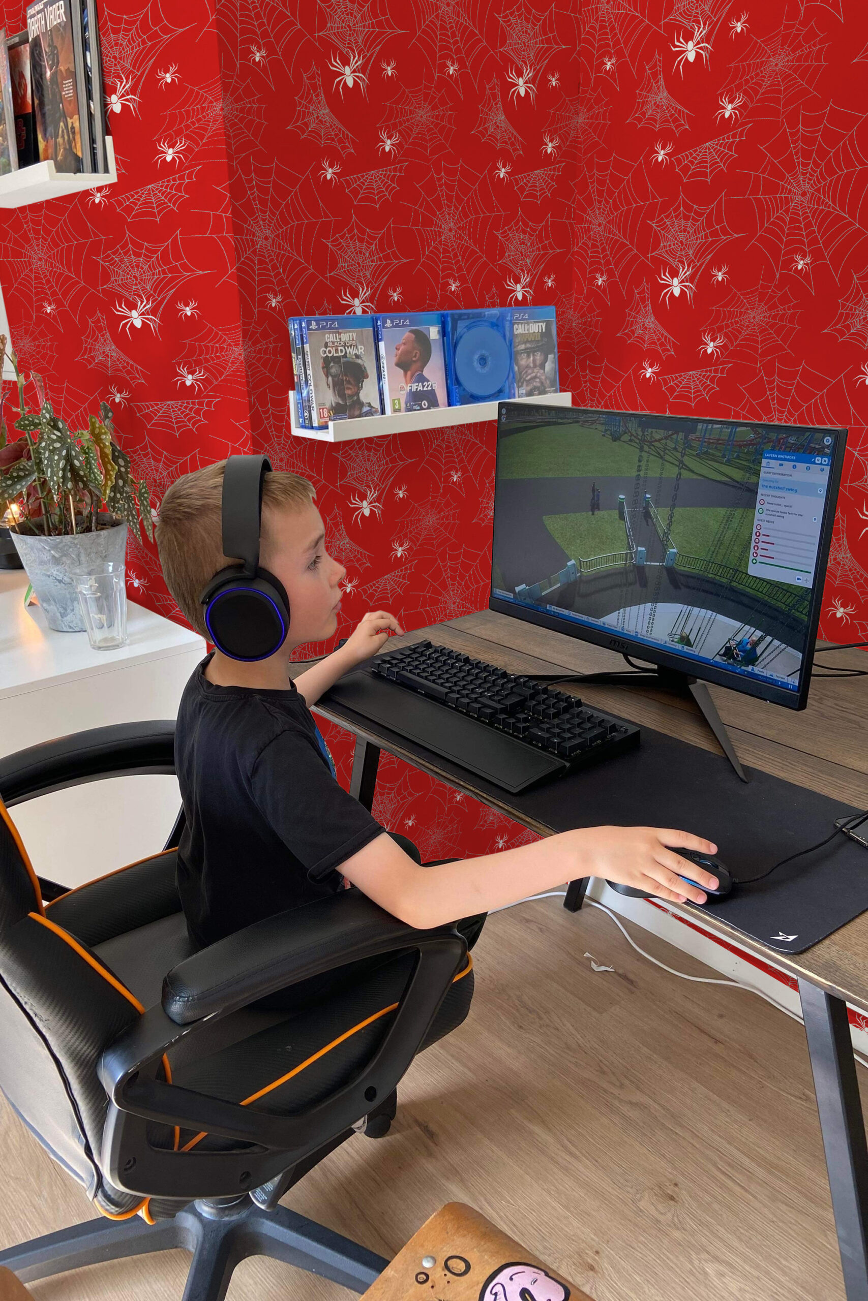 Bold Red Spider pre-pasted wallpaper with white spiderwebs and spiders covering the wall behind a gaming desk setup.