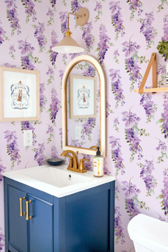 Delicate Purple Wisteria peel and stick wallpaper with cascading violet blooms covers the bathroom wall behind the sink.