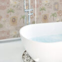 Whimsical Beige Lotus peel and stick wallpaper with lotus blooms, palms, and ornate frames on a beige wall behind a bathtub.