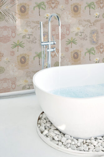 Whimsical Beige Lotus peel and stick wallpaper with lotus blooms, palms, and ornate frames on a beige wall behind a bathtub.