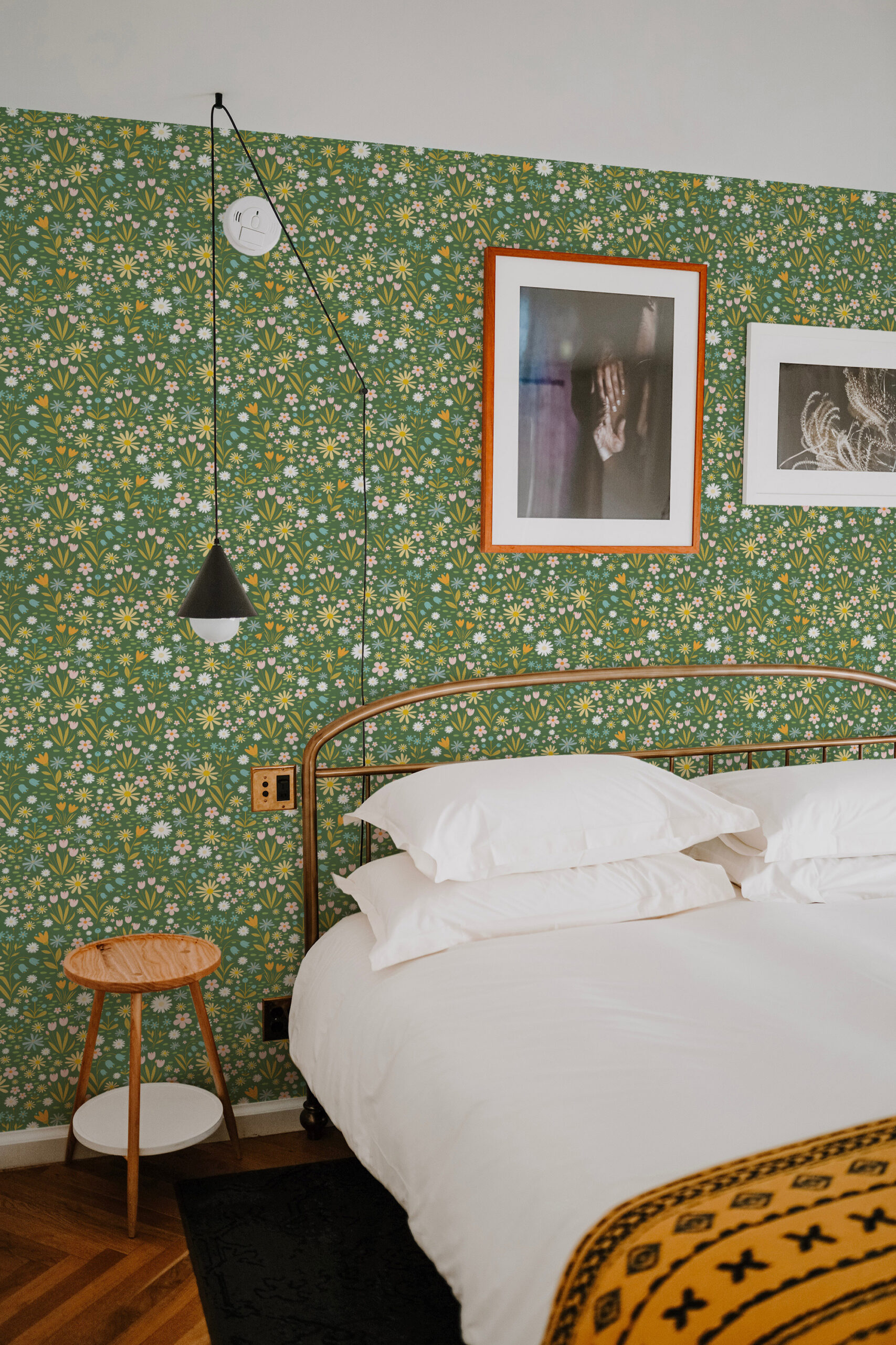 Playful Floral non-pasted wallpaper with tiny wildflowers on a green wall behind a bed and framed art.