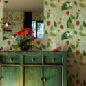 Cute, whimsical, strawberry stick wallpaper with red strawberries, green leaves, and small white flowers behind a wall mirror.