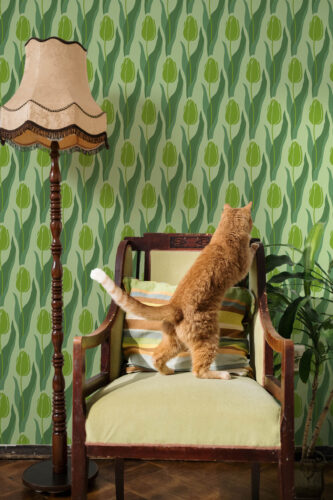 Seamless Green Tulip peel and stick wallpaper with repeating tulip buds and wavy leaves in layered green tones behind a chair.