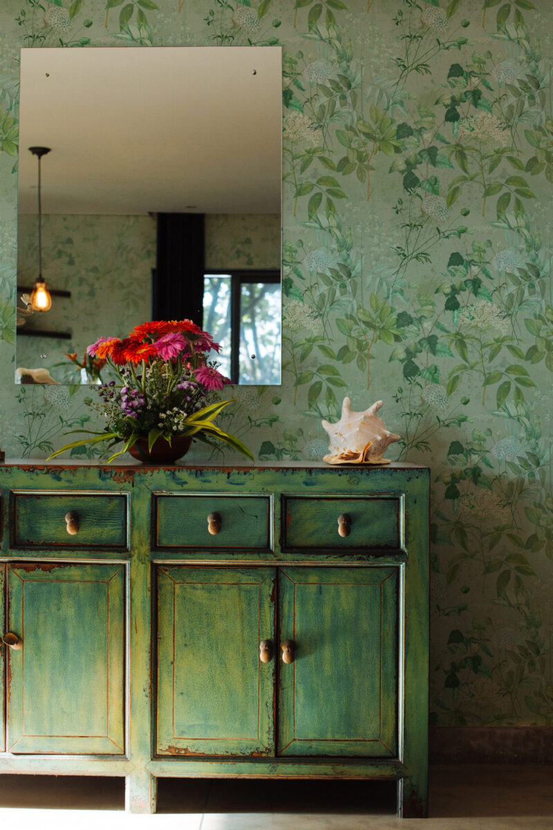 Green cabinet against a botanical wallpaper with foliage