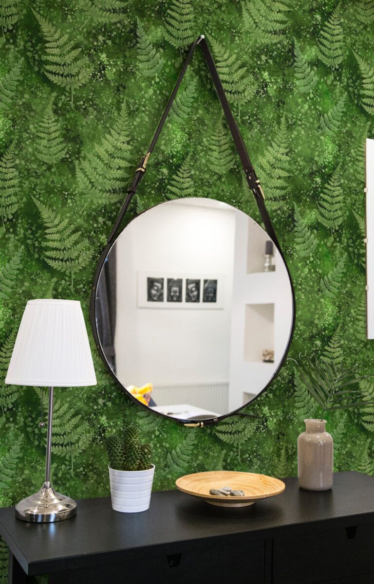 Green Moss and Fern peel and stick wallpaper with layered fern fronds and speckled green wash behind a round hanging mirror.