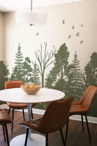 Sage Green Forest Scene peel and stick wall mural with silhouetted trees and flying birds across a dining room wall behind a table.