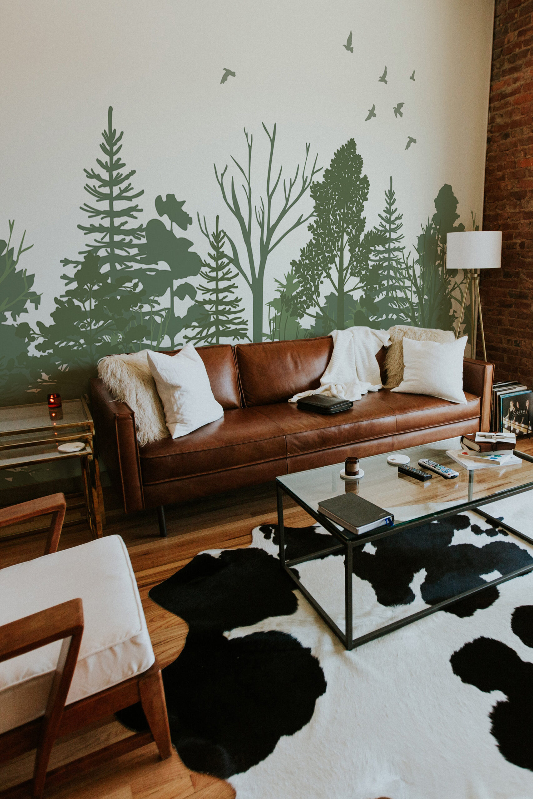 Sage Green Forest Scene self-adhesive wall mural in a living room, showing layered tree silhouettes and birds across the full wall.