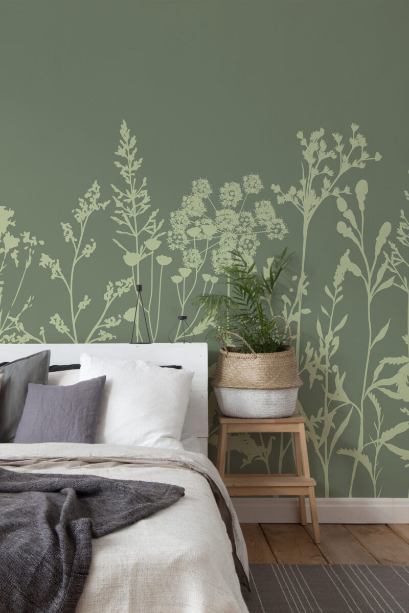 Green Meadow Wildflowers peel-and-stick wall mural behind a bed, showing pale wildflower silhouettes across a muted green wall.