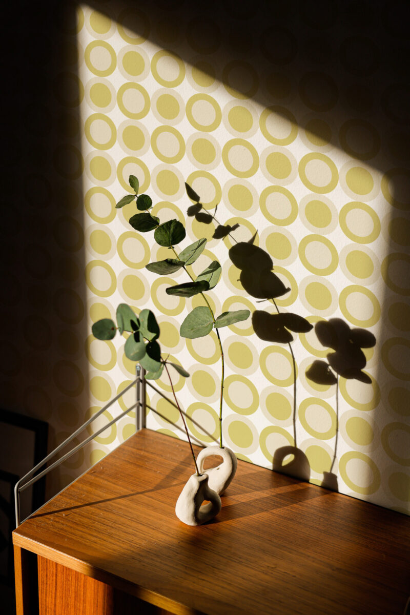 Retro Green Circle Dot pre-pasted wallpaper with repeating olive ring dots on a cream wall behind a small wooden table.