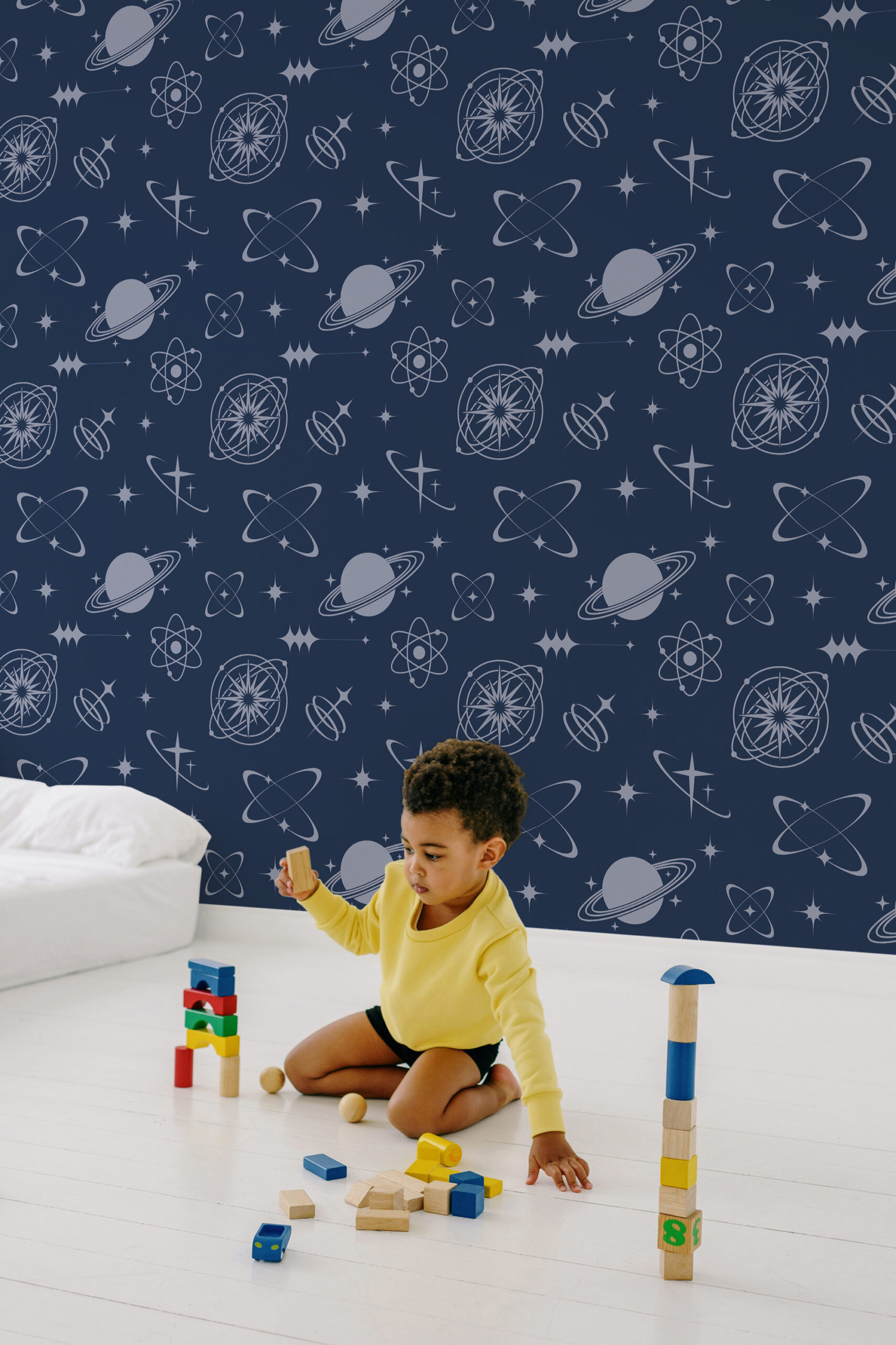 Retro Navy Blue Celestial non-pasted wallpaper with planets, stars, and atomic icons on a navy wall behind a child at play.