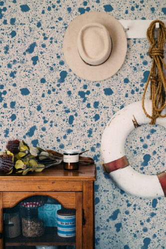 Dense Blue Splatter peel and stick wallpaper with scattered ink-like blue specks across the wall behind a hanging hat.