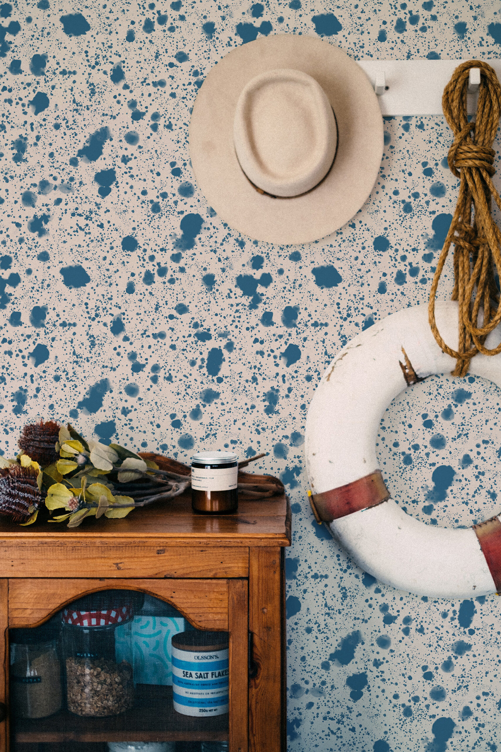 Dense Blue Splatter peel and stick wallpaper with scattered ink-like blue specks across the wall behind a hanging hat.