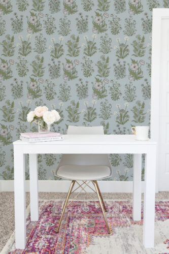 Fine Blue Wildflower peel and stick wallpaper with scattered pink blooms and green meadow stems on a soft blue wall.