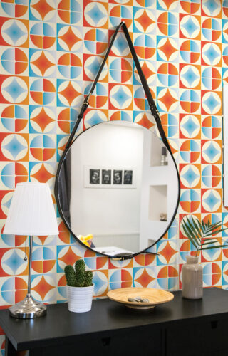 Retro Blue Orange Tile peel and stick wallpaper with a colorful geometric tile grid behind a round hanging mirror.