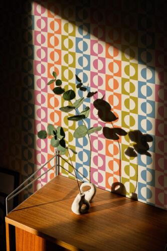 Retro Multicolored Split Circle shows a pastel checkerboard of half circles on peel and stick wallpaper behind a wood side table.