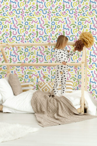 Bold White Squiggle peel and stick wallpaper with colorful squiggles and dots covering the wall behind a wooden canopy bed.