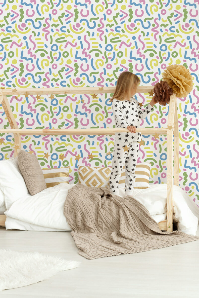 Bold White Squiggle peel and stick wallpaper with colorful squiggles and dots covering the wall behind a wooden canopy bed.