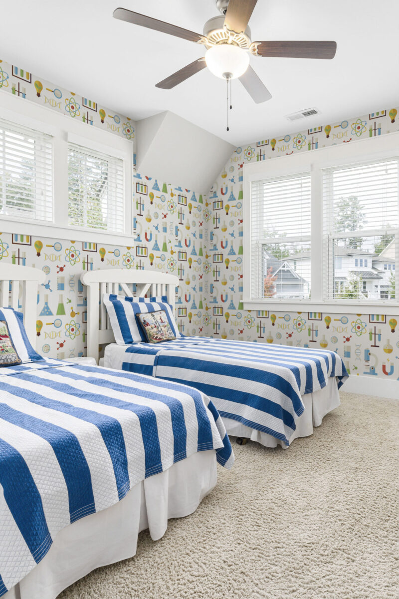 Playful White Science pre-pastedwallpaper with colorful lab icons covers the walls of a bedroom with twin beds.