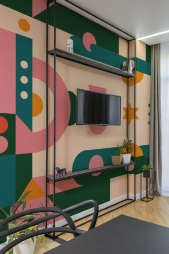 Retro Geometric Star peel and stick wall mural covers an accent wall with bold green, pink, and orange shapes behind a TV unit.