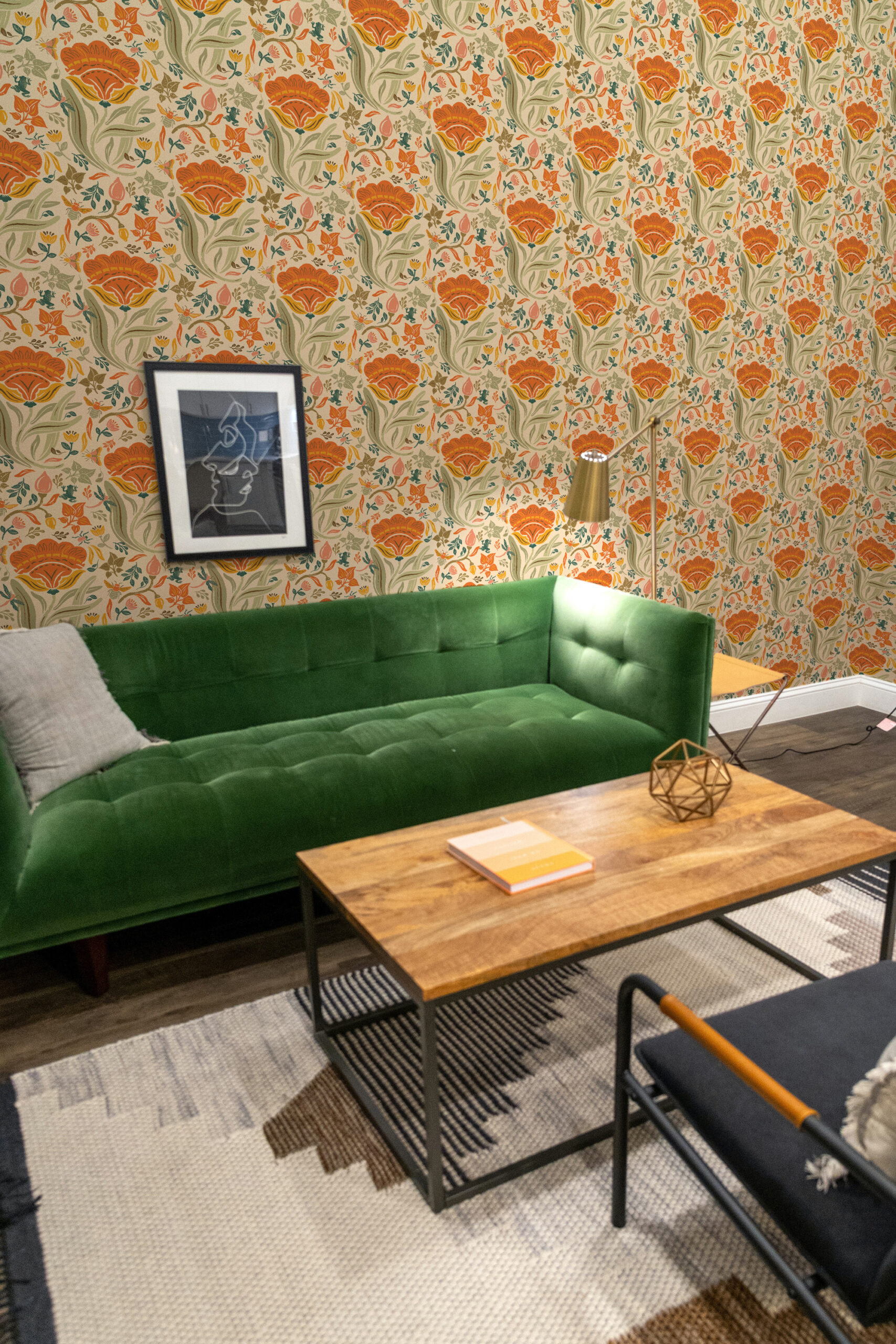 Bold Beige Floral self-adhesive wallpaper with orange blooms and leafy stems behind a green sofa in a living room.