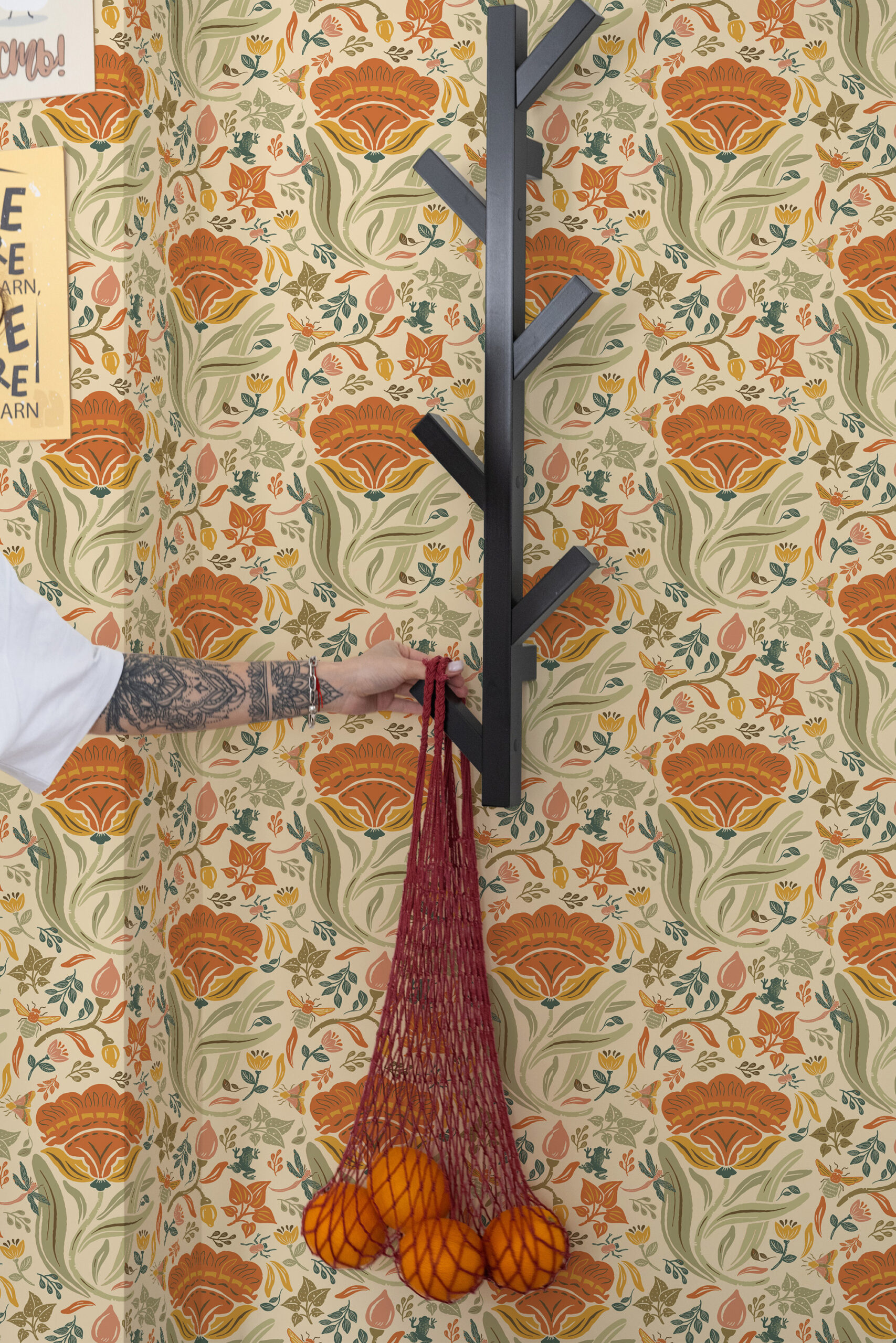 Bold Beige Floral pre-pasted wallpaper with orange blooms and leafy vines, shown behind a black wall coat rack.