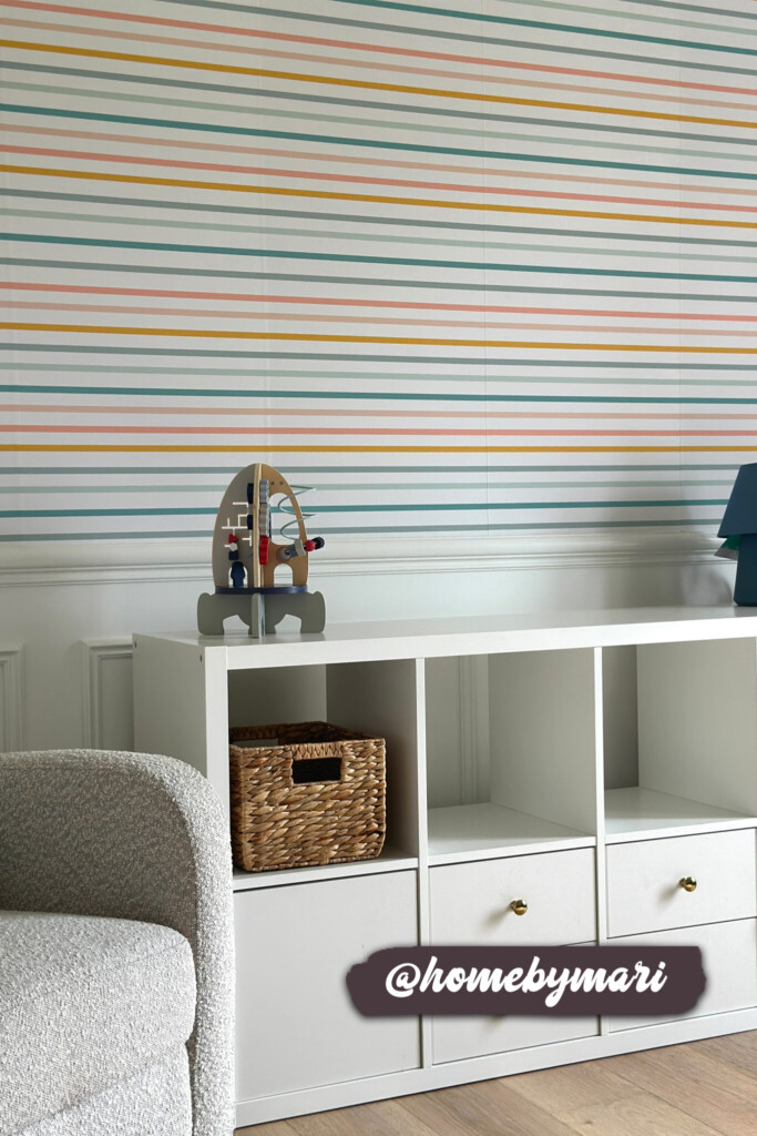 Modern striped wallpaper in soft pastel tones of blue, orange, and pink, complementing a minimalist children's room with white furniture and a wooden basket