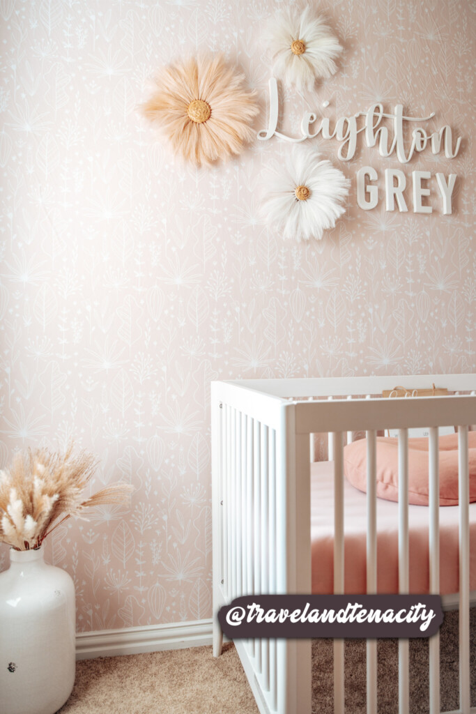 Soft blush floral wallpaper adds a delicate and serene touch to the nursery, complementing the white crib and personalized wall decor for a cozy, elegant ambiance