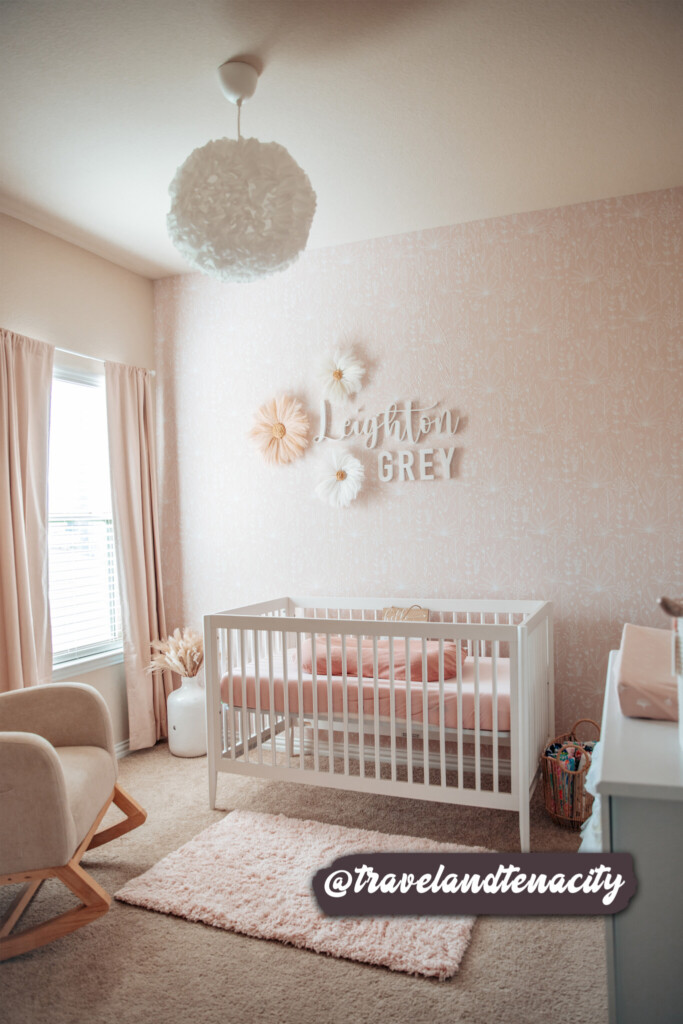 Subtle botanical wallpaper in a pastel pink shade creates a charming backdrop for a baby's room, harmonizing beautifully with natural textures and minimalist furniture