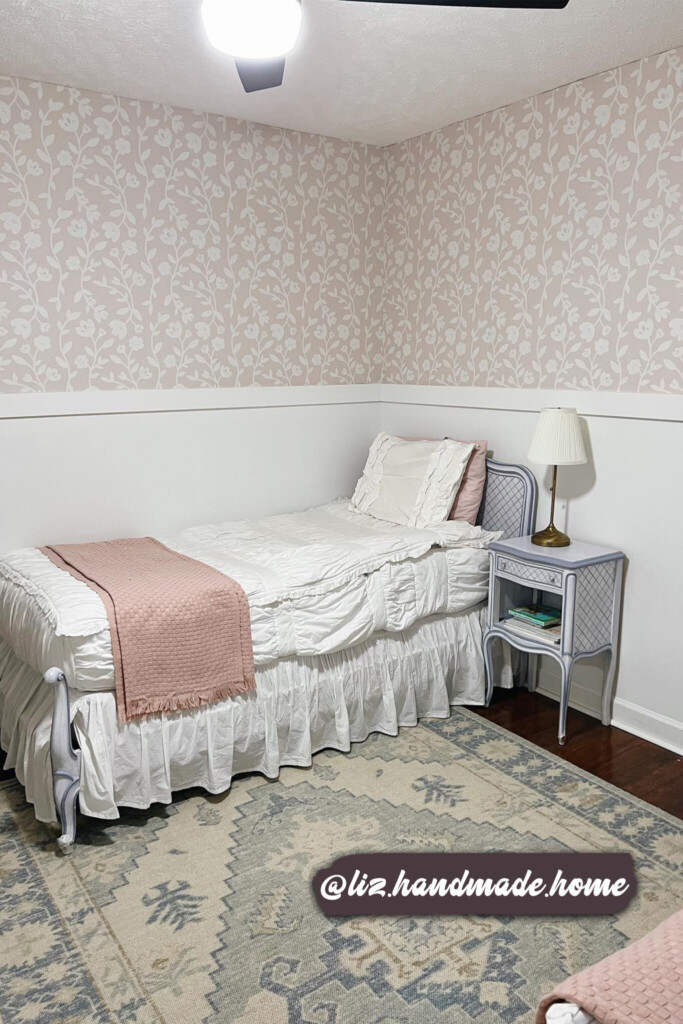 Elegant floral wallpaper in pale pink and white, creating a serene and charming atmosphere in a cottage-style bedroom with a ruffled bedspread and pastel accents