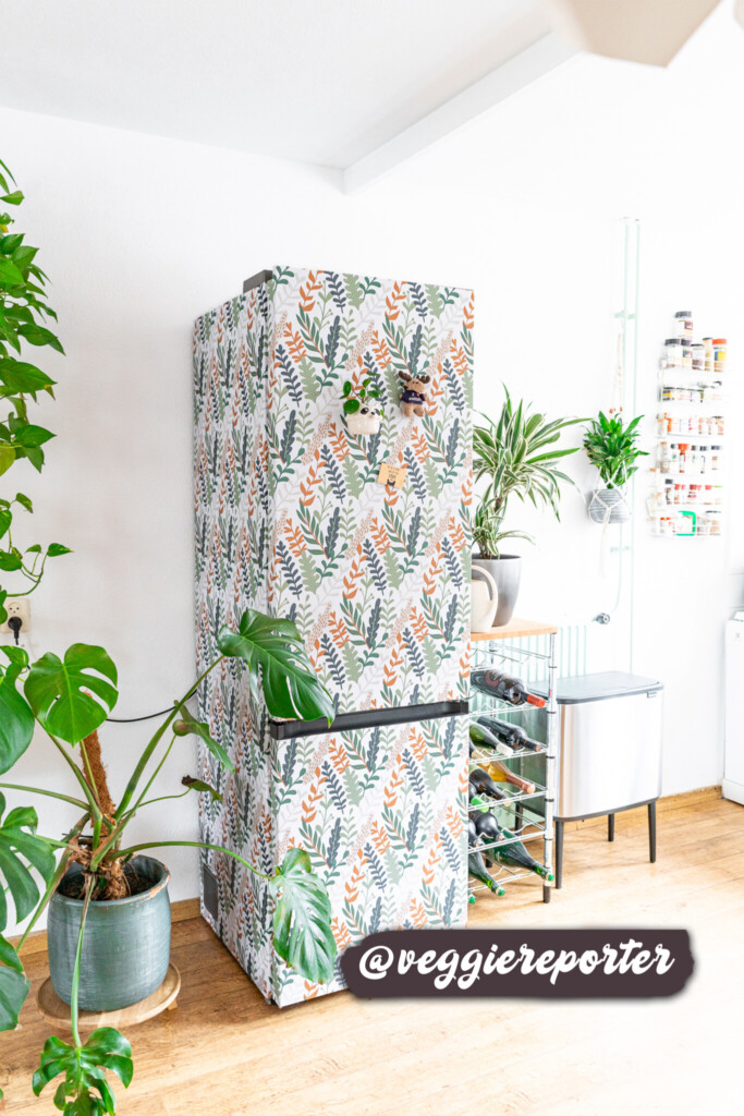 A kitchen fridge adorned with a nature-inspired wallpaper featuring colorful foliage patterns, seamlessly blending with the greenery and creating a cozy, organic atmosphere